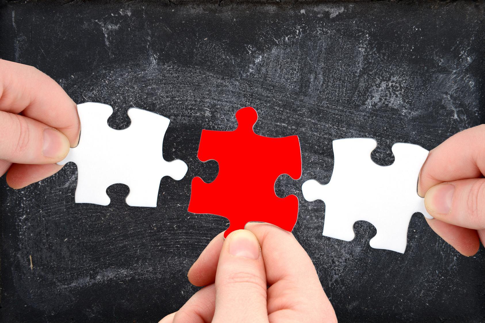 © Gerhard Seybert Das Bild zeigt, wie drei Hände Puzzleteile zusammenfügen, wobei ein rotes Teil die beiden weißen Teile verbindet. Es symbolisiert Zusammenarbeit und Problemlösung.